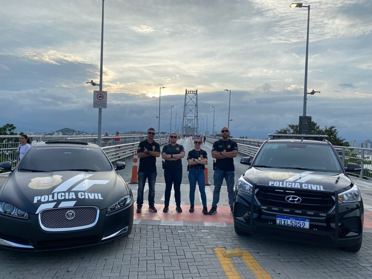 Ponte Hercílio Luz de fundo, na frente quatro policiais e duas viaturas da Polícia Civil