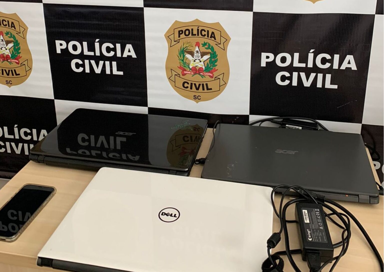 3 Notebooks e 1 celular encima de uma mesa, no fundo um banner