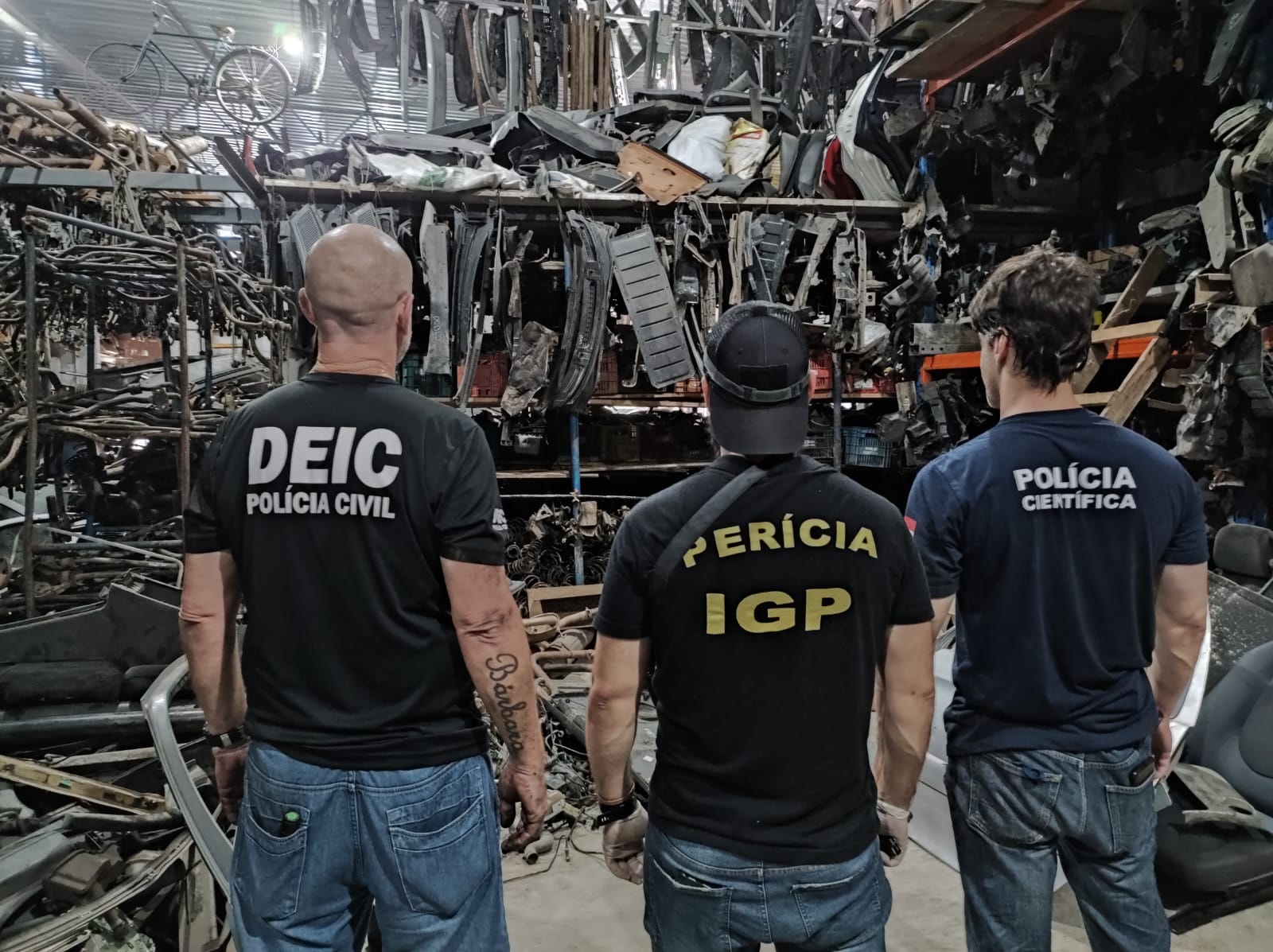 agente da DEIC, IGP e Policia Cientifica de costas em frente a partes desmembradas de carros