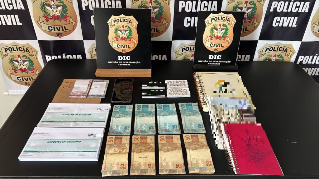 BANNEER DA PC DE FUNDO, DOIS POSTERES DA DIC, DINHEIRO, ENVELOPE PARA DEPOSITAR NO BANCO, TRÊS CADERNOS, CARTÕES DE JOGO E CARTÃO DE VISITA