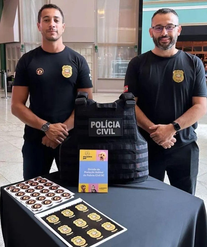 Policiais civis em pé atrás de uma mesa e sobre ela adesivos da policia civil mirim