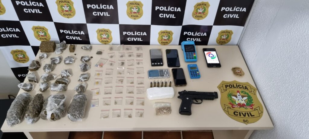 banner da policia civil e mesa com drogas apreendidas, celulares e balança