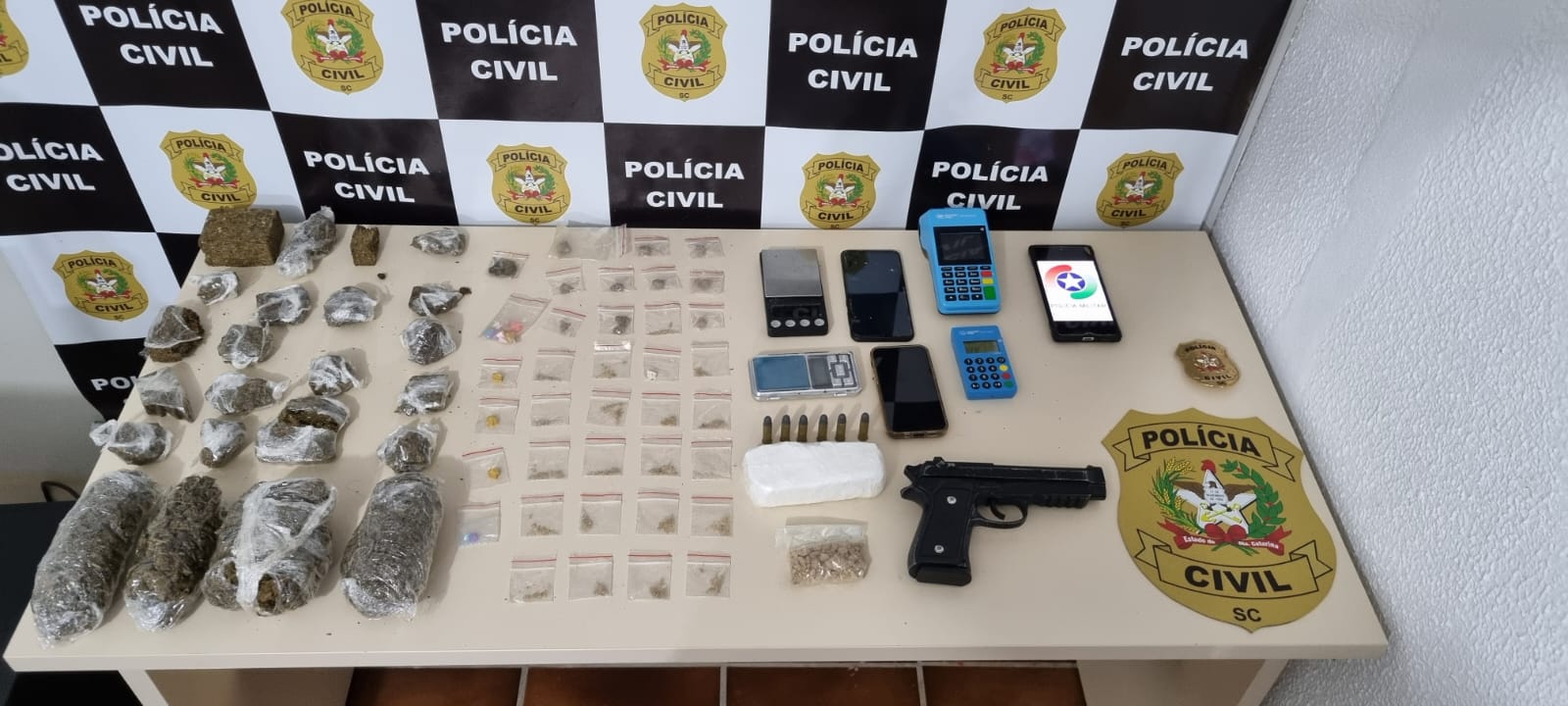 banner da policia civil e mesa com drogas apreendidas, celulares e balança